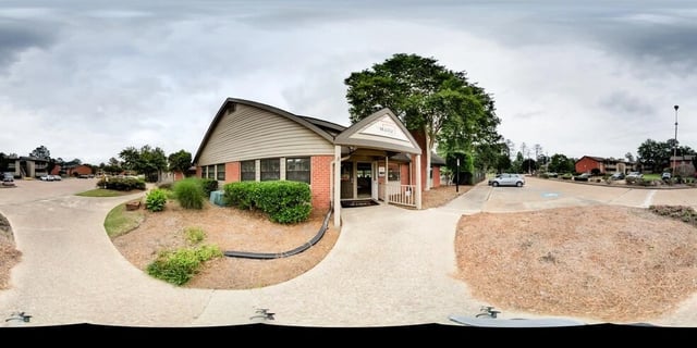 Exterior view of the apartment complex with a modern office building entrance and parking area.