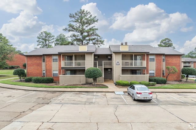 Exterior of a brick and tan apartment building with a parking lot in front.