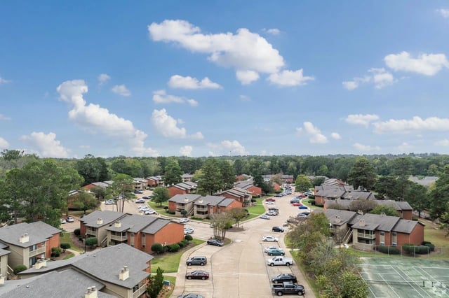 Aerial view of a multi-building apartment complex with parking lots and trees.