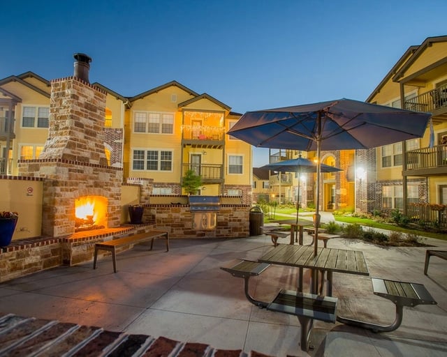 Outdoor patio with a stone fireplace, grill, picnic tables, and umbrellas.