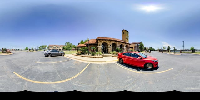 Exterior view of apartment building entrance with parking lot and cars.