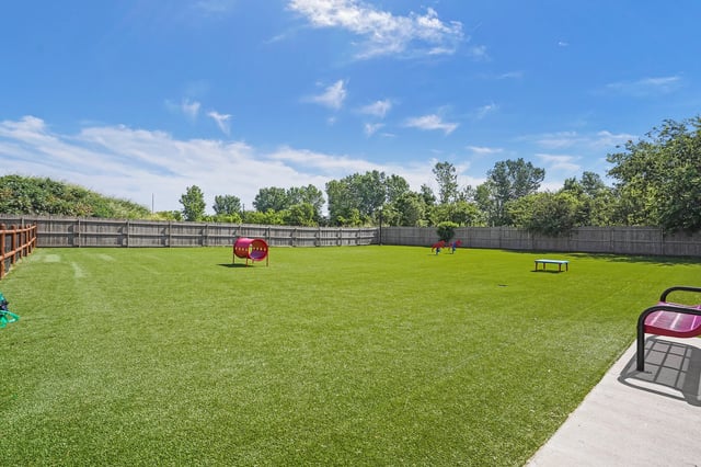 Open grassy community lawn with a small playground and surrounding wooden fence.