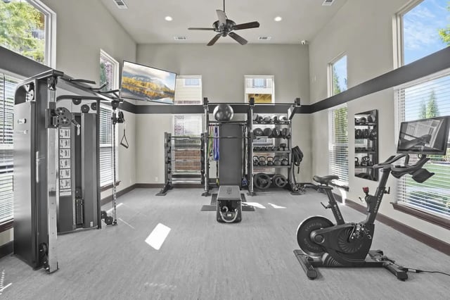 Bright community gym with weight machines, free weights, cardio bike, and large windows.