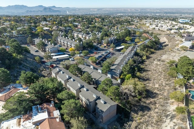 Aerial view of apartment buildings with surrounding trees and distant mountains.