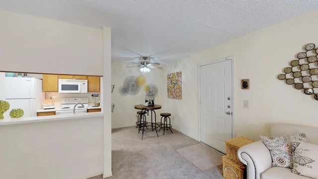 Living room and kitchen area with a small dining table and stools, and a white couch.