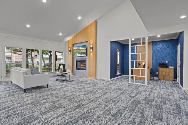 Spacious community lounge area with a white sofa, fireplace, TV, and a workspace.