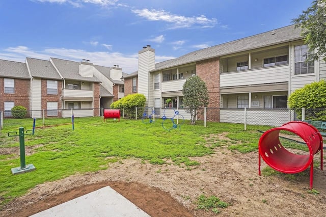 Outdoor community courtyard with a playground and apartment buildings in the background.