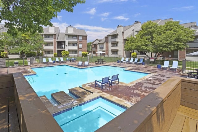 Outdoor community pool with blue water, lounge chairs, and surrounding apartment buildings.