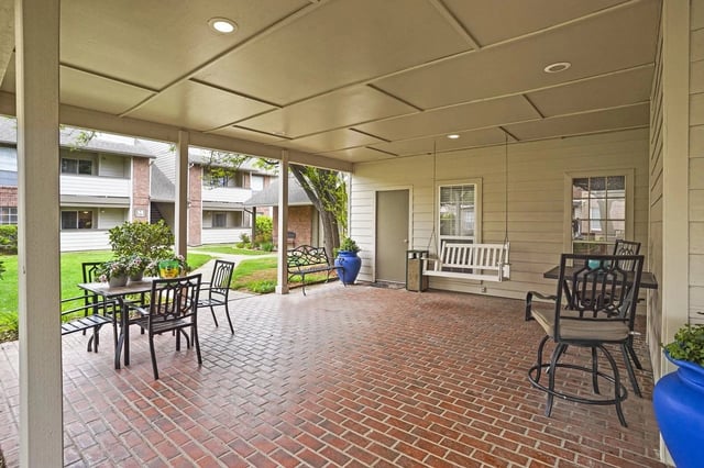 Covered brick patio with outdoor seating and a hanging porch swing in a courtyard.