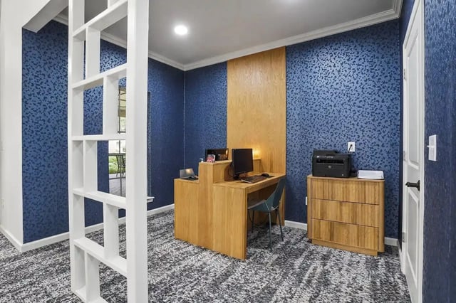 Interior apartment office with wood desk, computer, and printer against blue patterned wallpaper.