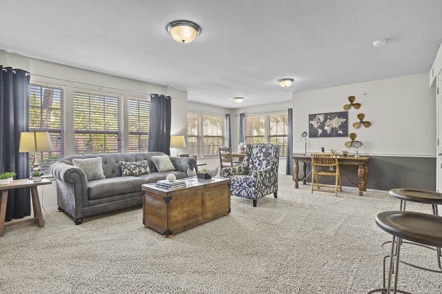 Living room in an apartment with a gray sofa, patterned chair, coffee table, and large windows.