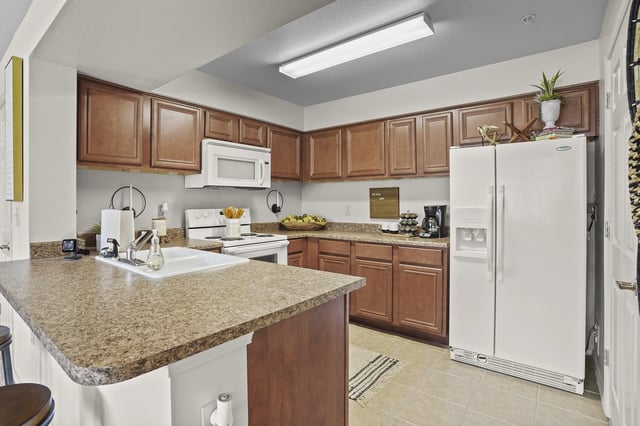 Apartment kitchen with brown wood cabinets, white appliances, and granite countertops.