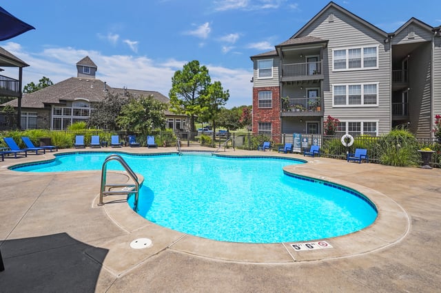 Outdoor swimming pool with lounge chairs and apartment buildings in the background.