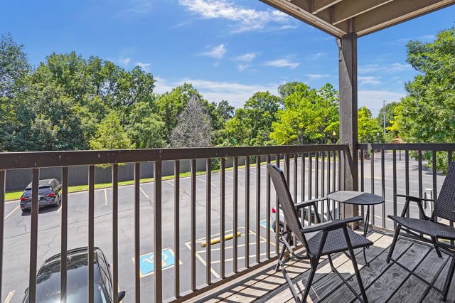 Balcony overlooking a parking lot with trees and a blue sky.