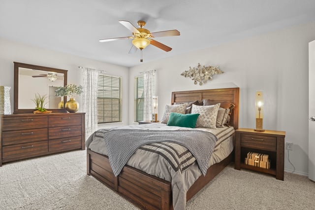 Queen-size bed with plush bedding and decorative pillows, dresser with mirror, nightstand, and ceiling fan.