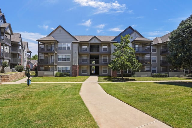 Exterior view of apartment buildings with a paved walkway and manicured lawn.