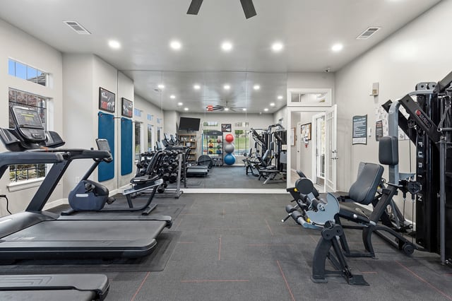 Interior view of a well-equipped apartment fitness center with treadmills, weight machines, dumbbells, and mirrors.