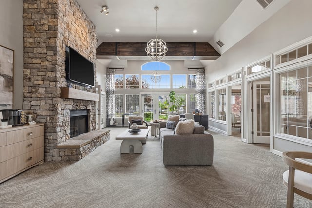Spacious community lounge with a stone fireplace, comfortable seating, and large windows.