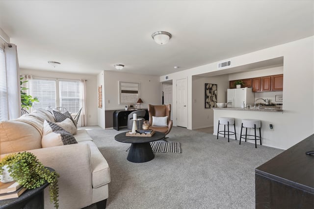 Living room and kitchen area with a sofa, armchair, coffee table, and bar seating.