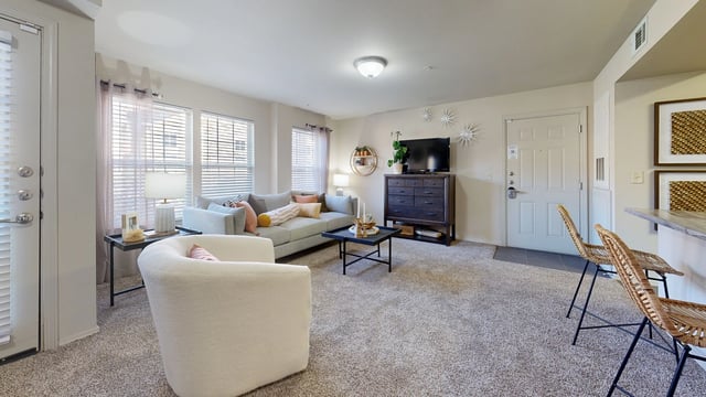 Bright and airy living room with a gray sofa, white armchair, coffee table, and TV stand.