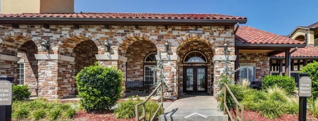 Exterior of the apartment building entrance with stone facade and arched walkways.