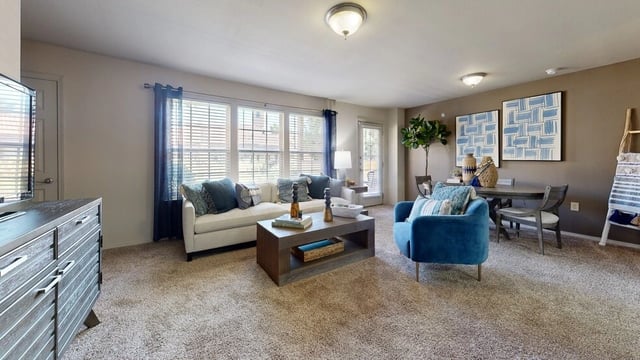 Living room with white sofa, blue accent chair, coffee table, dining table, and TV stand.