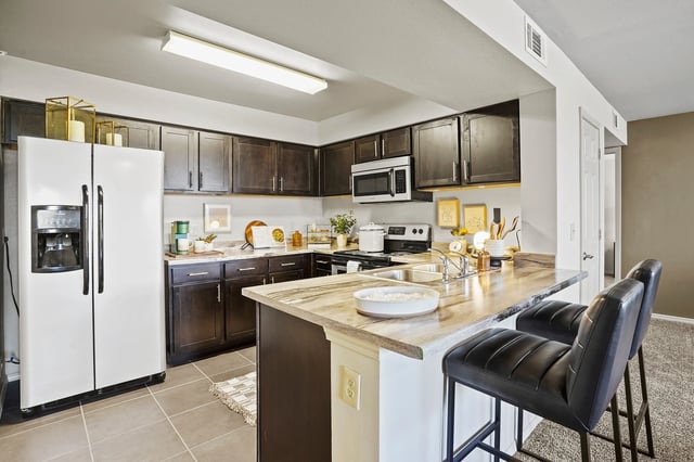Modern kitchen with dark wood cabinets, granite countertops, stainless steel appliances, and a breakfast bar with seating.