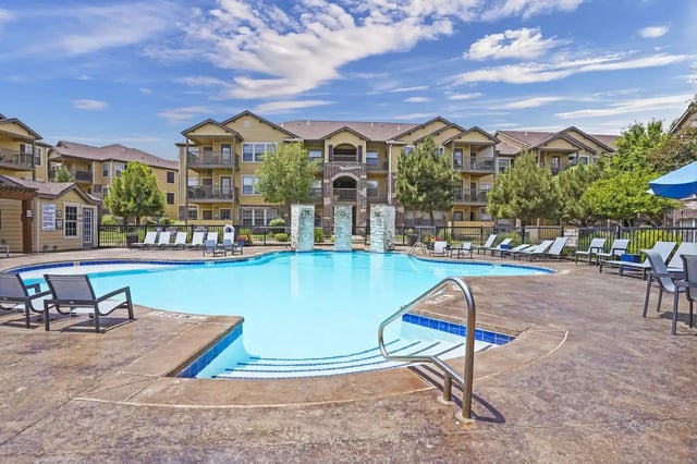 Resort-style swimming pool with lounge chairs and surrounding apartment buildings.