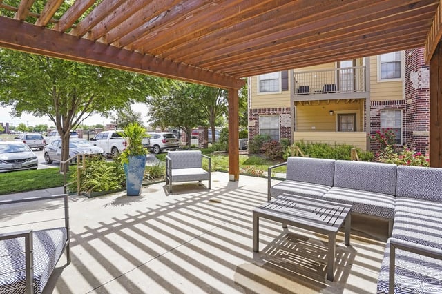 Outdoor covered patio seating area with a pergola, sofa, chairs, and coffee table.