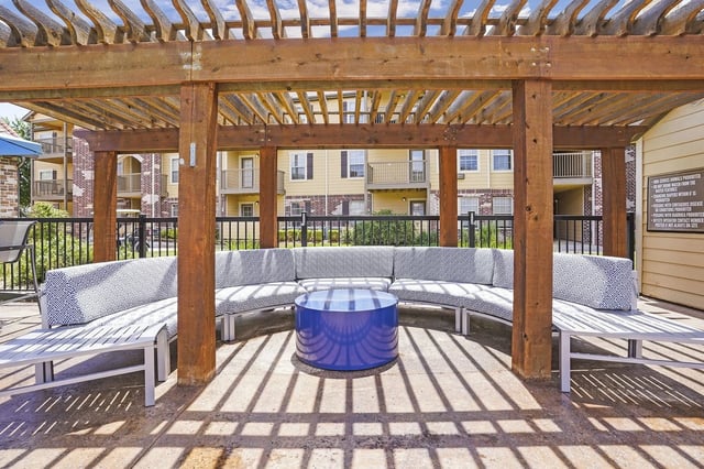 Outdoor lounge area with sectional seating and a blue coffee table under a wooden pergola.
