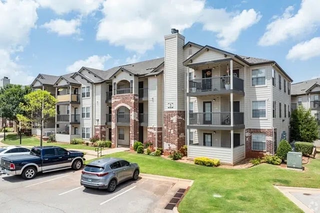 Exterior view of a multi-story apartment complex with balconies and a parking lot.