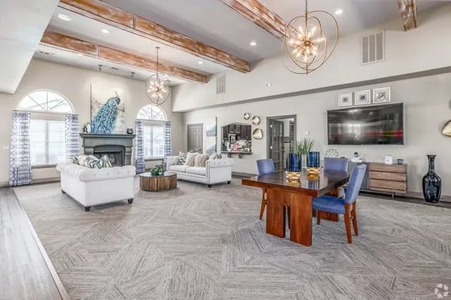 Bright community lounge with sofas, a dining table, large arched windows, and a wall-mounted TV.