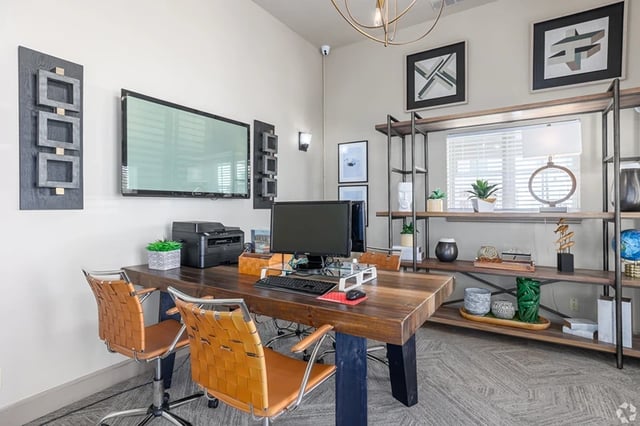 Home office setup with a wooden desk, orange chairs, computer, and shelving.
