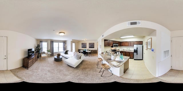 Open concept living room and kitchen with white sectional sofa, TV, dining table, and kitchen island.