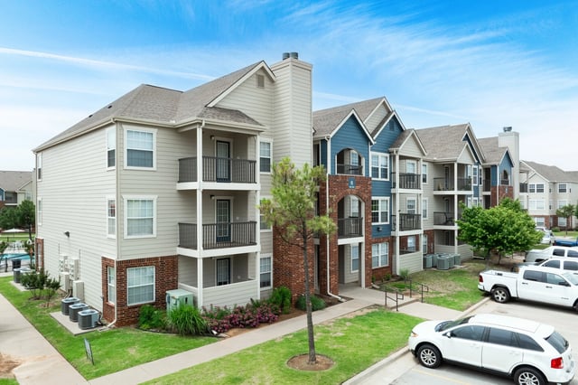 Exterior view of apartment buildings with balconies and parking lot.