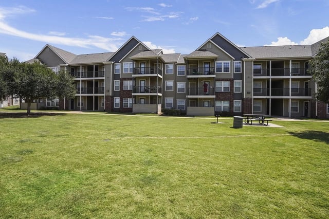 Exterior view of a multi-building apartment complex with balconies and a large grassy lawn.
