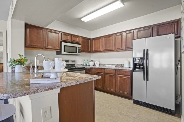 Kitchen in an apartment with dark wood cabinets, granite countertops, and a stainless steel refrigerator.