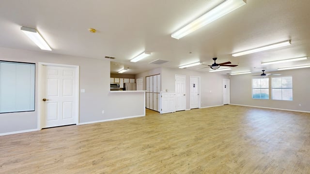 Spacious community room with wood-look flooring, a kitchen counter, and multiple doors.