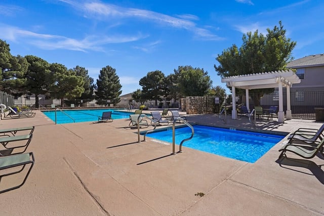 Resort-style swimming pool and lounge chairs at apartment complex on a sunny day.