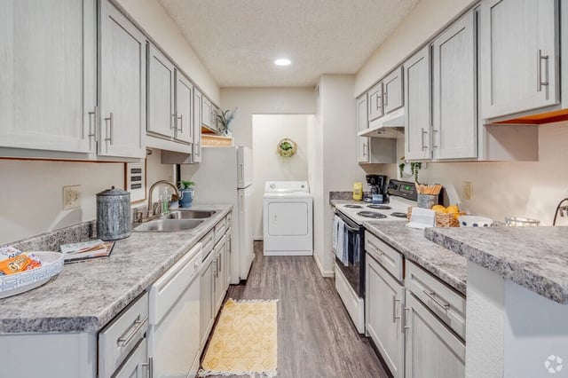 Kitchen with white cabinets, granite countertops, stainless steel sink, dishwasher, refrigerator, and a washer and dryer.