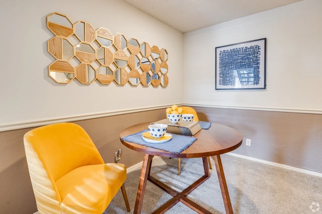 Round dining table with yellow chairs and decorative wall mirror.