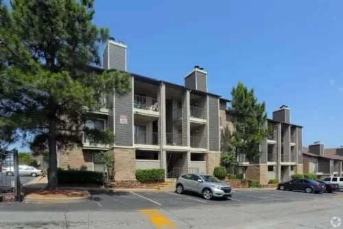 Exterior view of a multi-story apartment building with a parking lot and trees in front.
