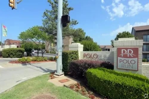 Exterior view of Polo Run apartment community entrance with sign and manicured landscaping.
