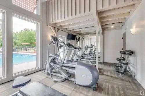 Fitness center with cardio equipment by large windows overlooking the pool.