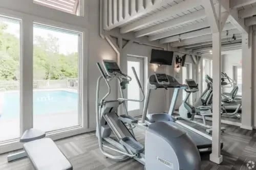 Indoor fitness center with treadmills and ellipticals by large windows.