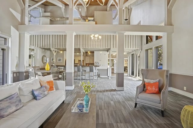 Open-concept community lounge with sofa, armchair, dining area, and visible kitchen.