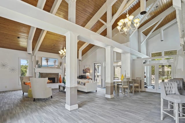 Bright community lounge with white columns, vaulted wood ceiling, and a fireplace.