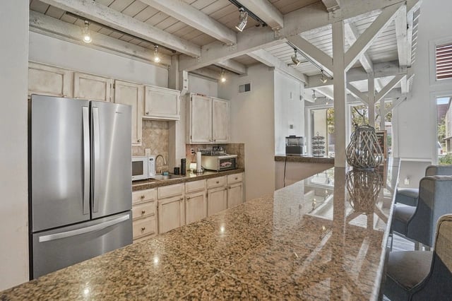 Open kitchen with granite countertops, a stainless steel fridge, and light wood cabinets.