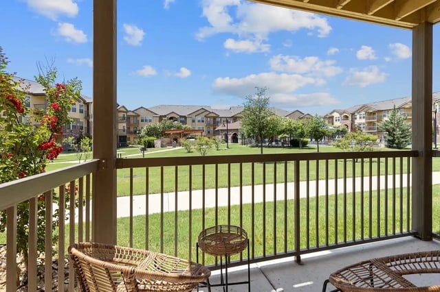 View of the community grounds from a balcony, showing buildings, a pool, and landscaping under a blue sky.