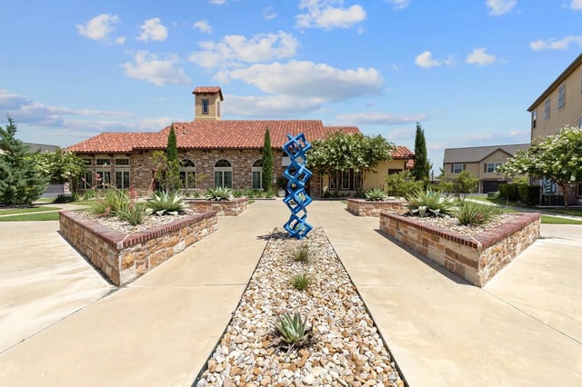Courtyard with a modern blue sculpture and landscaped planters in front of a building with a terracotta roof.